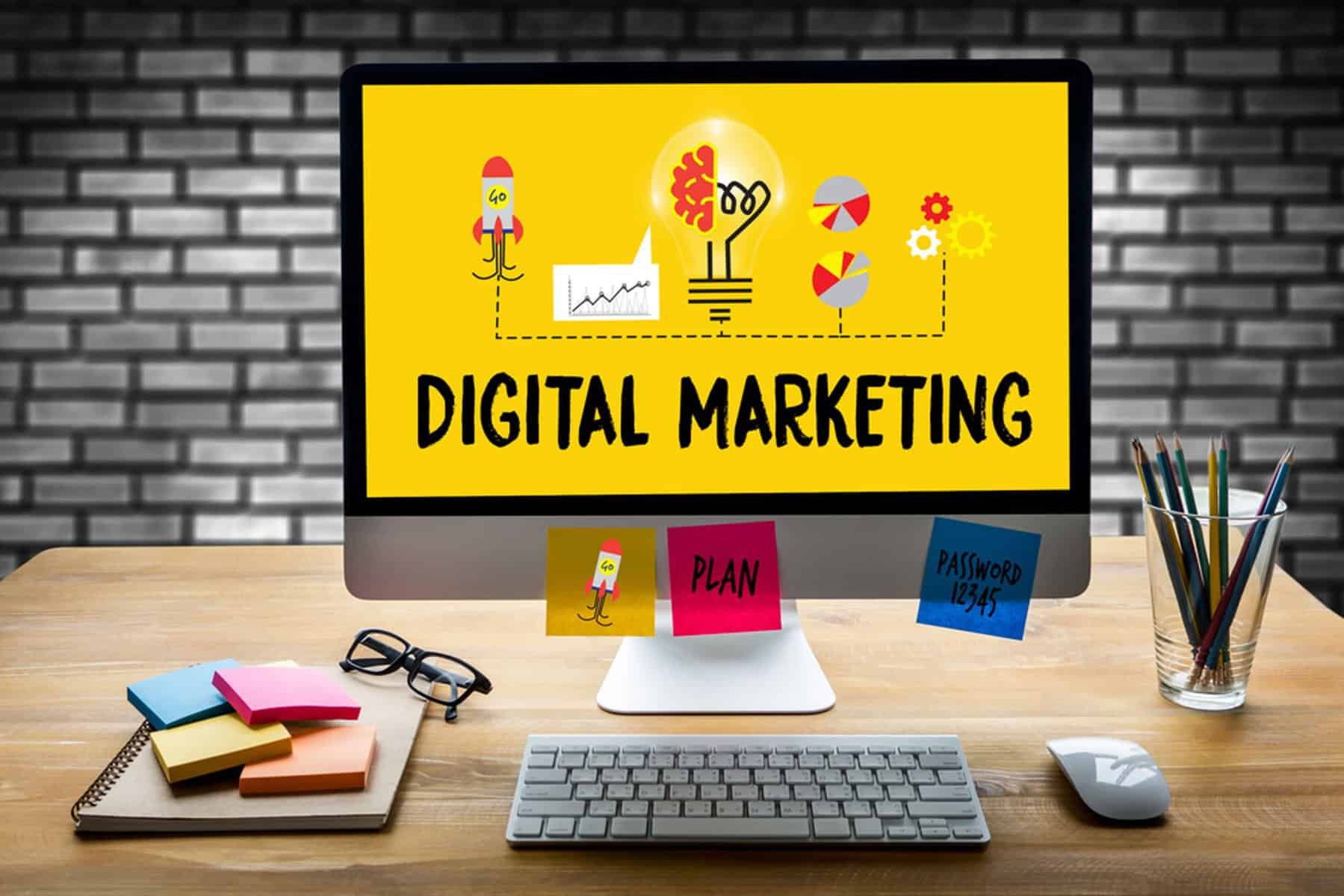 Photo of desk with a screen that has the words "DIGITAL MARKETING" below an infographic illustration.